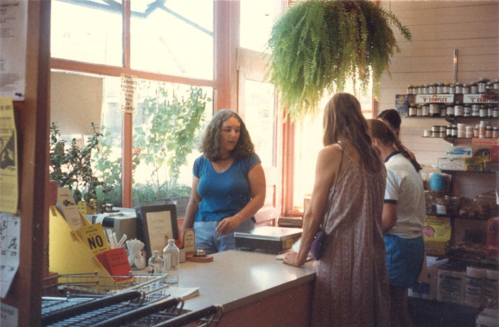 Joyce serving a shopper at People's Food Co-op checkout in the late 1980s